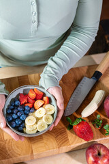 Woman holding a bowl of fresh fruit in the kitchen (top view)