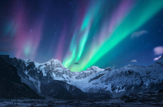 Northern lights over the snowy mountains at night in Lofoten, Norway. Aurora borealis above the snow covered rocks. Winter landscape with polar lights, mountain peak. Beautiful starry sky with aurora	