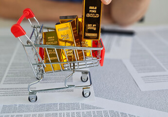 Buying gold bars in a shopping cart on financial papers during market analysis concept
