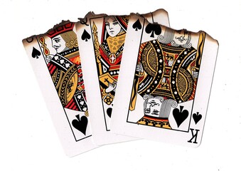 A hand of three partly burnt playing cards in the suit of spades.