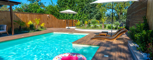 Modern backyard swimming pool with turquoise water, wooden deck, lounge chairs, umbrellas, and pink...