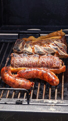 Close view of a barbecue on the grill, with large pieces of jucy beef and chorizos