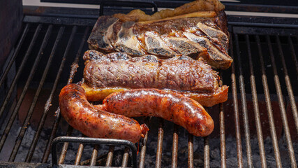 Close view of a barbecue on the grill, with large pieces of jucy beef and chorizos