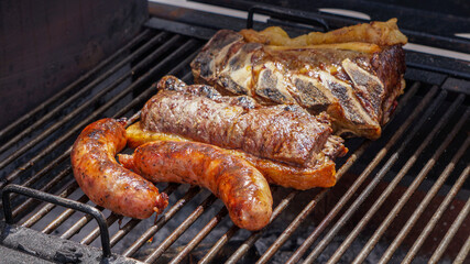 Close view of a barbecue on the grill, with large pieces of jucy beef and chorizos