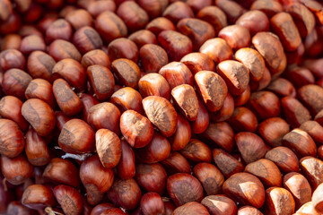 Large pile of unprocessed chestnuts with rich brown tones and matte rough patches densely packed together