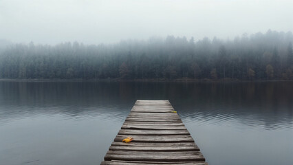 Naklejka premium A mysterious and serene morning scene of a wooden dock extending into a foggy lake. The misty atmosphere adds a sense of tranquility and solitude.