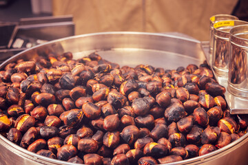 Large metal tray filled with freshly roasted chestnuts cracked shells reveal golden interiors warm steam rises enhancing the rich aroma of this seasonal delicacy