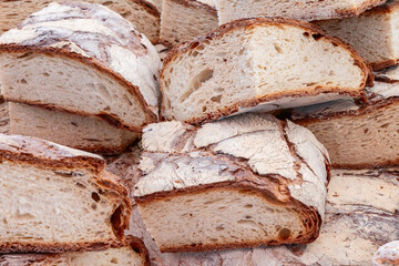 Background of sliced rustic bread with a thick crust golden-brown edges contrast with the airy porous crumb highlighting its traditional artisanal texture