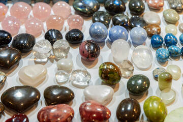 Assorted tumbled gemstones of different shades and patterns featuring translucent clear stones and opaque minerals arranged in a decorative display under bright lighting
