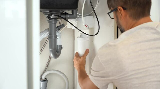Replacement water purifier. Plumber installs water filter. Man changes water filter cartridges in kitchen under kitchen sink