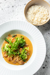 A delicious plate of creamy seafood curry garnished with fresh greens, served alongside a bowl of fluffy white rice on a textured gray surface.
