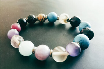 A colorful bracelet made of various gemstones rests on a smooth dark surface, highlighting the beauty of natural stones with diverse hues and patterns.