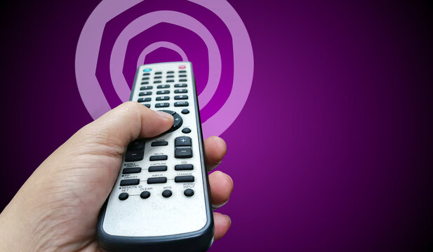 A hand confidently holds a remote control against a vibrant purple background, blending modern technology with a bold and energetic aesthetic.