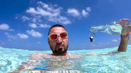 A person is underwater in the Maldives, partially submerged with a glass bottle and clear blue water above.