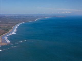Coastal landscape with waves rolling onto sandy shore under clear blue sky