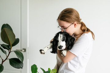 Blonde-haired girl distracted from her tasks, kissing the Spaniel puppy she is holding in her arms