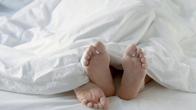 Passionate Loving couple having sex under white blanket in bedroom Close up of male and female feet on bed 