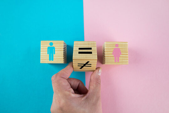 Gender equality symbol. Hand turns cube and changes inequality sign to equal sign between male and female symbols. Nice pink and blue background