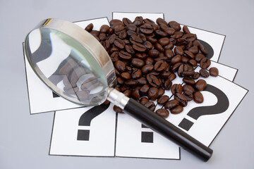 Roasted coffee beans on question marks under magnifying glass. Coffee FAQ concept.