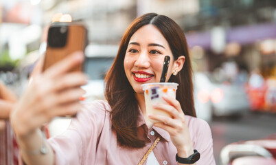 Happy adult asian traveler woman eating taiwan boba dessert and take selfie for social media
