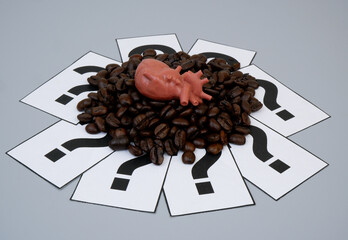 Roasted coffee beans on question marks and human heart model. Coffee affects heart health concept.	