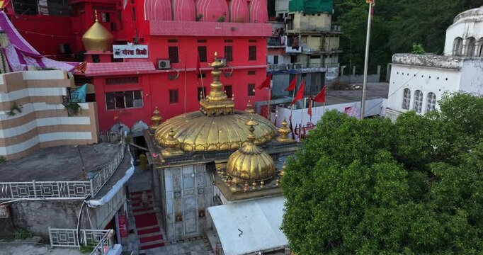 A top view of the Jwalamukhi Temple reveals its golden dome, as the drone moves away, showcasing the entire temple campus while the camera slowly tilts up to capture the surrounding area.