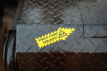 Pinch point warning sign in yellow arrow on metal surface that point to the hazard (English and Indonesian text). Safety sign and symbol for industrial safe working concept.