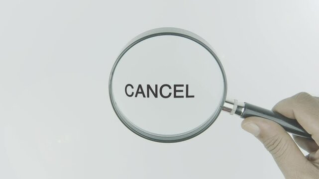 Cancel text or word highlighted by a magnifying glass in a hand on a white background, symbolizing termination, stoppage, and cancellation