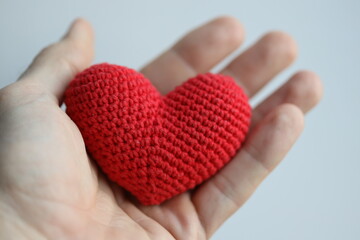 A close-up of a hand holding a crocheted red heart, symbolizing love and affection.