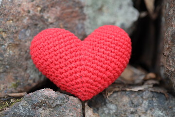 A bright red crocheted heart sits atop a pile of rugged rocks, perfect for Valentine's Day or a...