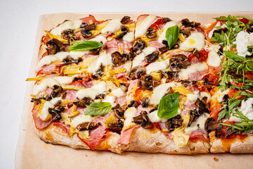 A hearty rectangular pizza topped with ham, mushrooms, and fresh basil tempts everyone
