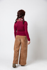 Woman standing, seen from behind, full body. She is wearing a red or burgundy jumper and brown trousers.
