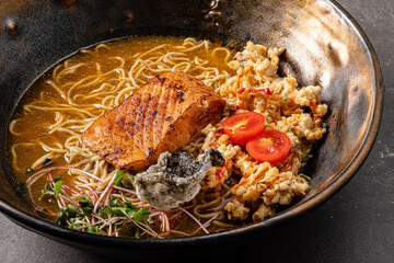 Enjoy a delectable ramen bowl featuring grilled salmon, cherry tomatoes, and unique crispy garnish