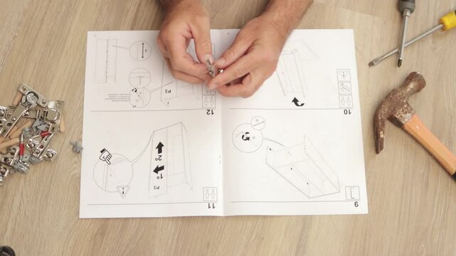 Skilled carpenter carefully reading instruction manual while methodically assembling wooden furniture using metal hardware like screws, bolts, and hinges at home workshop