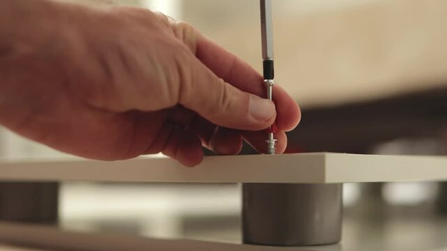 Professional furniture assembler carefully securing white shelf to mounting support, systematically tightening screws with precision screwdriver for stable furniture installation