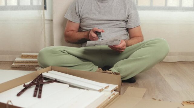 Professional carpenter carefully assembling flat pack furniture, methodically following manual instructions while using various tools and components inside modern home interior