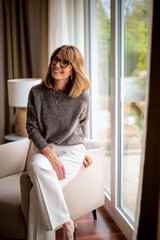Blond haired woman wearing casual clothes and relaxing by the window