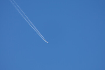 Airplane in a blue sky without clouds. The airplane has a flight trail behind it