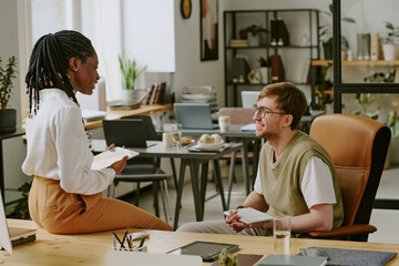 Wide shot of young programmers holding tablets while having nice conversation during lunch break in office