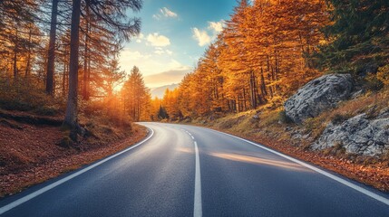 Fototapeta premium Mountain road in an autumn forest at sunset in Italy A scenic asphalt roadway lined with orange foliage sunlight a blue sky and high rocks Fall landscape featuring an empty highway