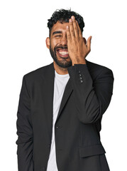 Hispanic businessman in suit in studio having fun covering half of face with palm.