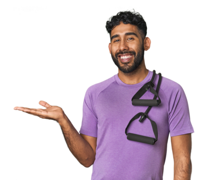 Hispanic male in sportswear with bands in studio showing a copy space on a palm and holding another hand on waist.