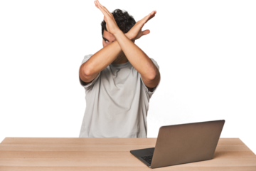 Hispanic young man working on laptop keeping two arms crossed, denial concept.
