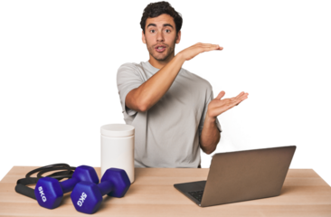 Hispanic trainer planning workout shocked and amazed holding a copy space between hands.