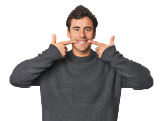 Young Hispanic man in studio smiles, pointing fingers at mouth.