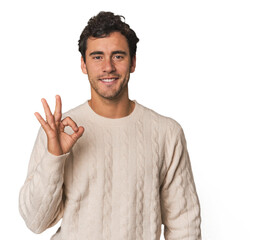 Young Hispanic man in studio cheerful and confident showing ok gesture.