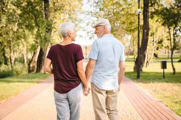 Rear view of senior couple walking outdoors in summer park and embracing, loving happy mature...