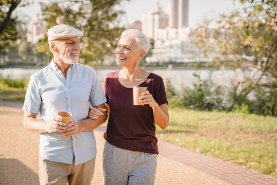 Romantic senior couple walking outdoors in summer park and embracing, loving happy mature spouses hugging and smiling to each other, cheerful husband and wife enjoying outside walk, copy space