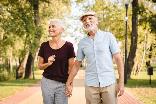 Side view of smiling senior couple family hugging while walking in summer city park enjoying retirement and spending time together in nature. Romance love care and elderly people relationship concept.