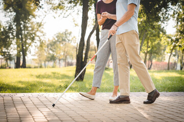 Cropped of elderly couple walking in the park. Senior man is blind and old woman helping him to...